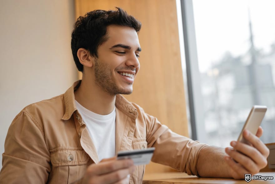 How to withdraw money from prepaid card online: man holding phone and card to illustrate prepaid card withdrawal to money app. How to withdraw money from prepaid card online: man holding phone and card to illustrate prepaid card withdrawal to money app.