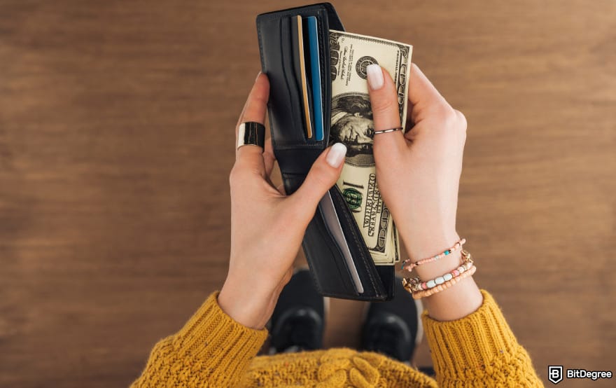 How to withdraw money from prepaid card online: woman holding USD bills to illustrate paying for prepaid card fees.