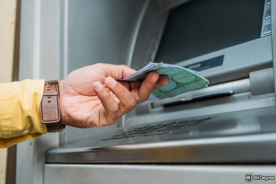 Is Bitcoin legal: a hand with a brown leather watch withdrawing bills from ATM.