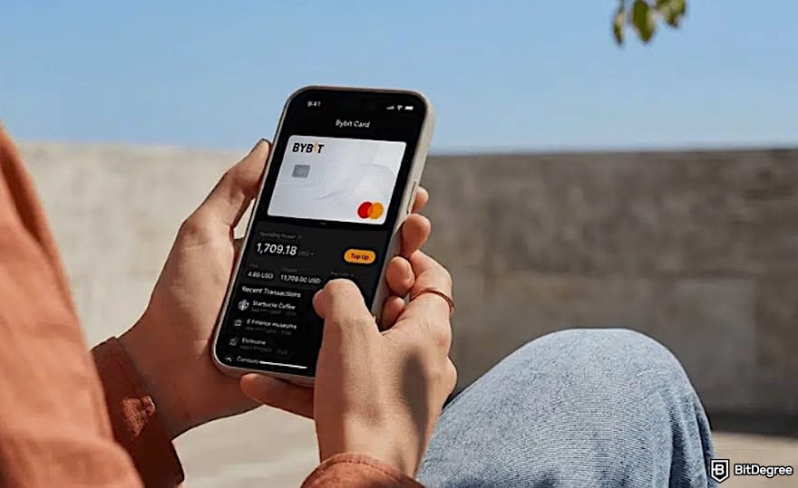 Is Bybit safe: someone holding a phone, showing Bybit Debit Card. Is Bybit safe: someone holding a phone, showing Bybit Debit Card.