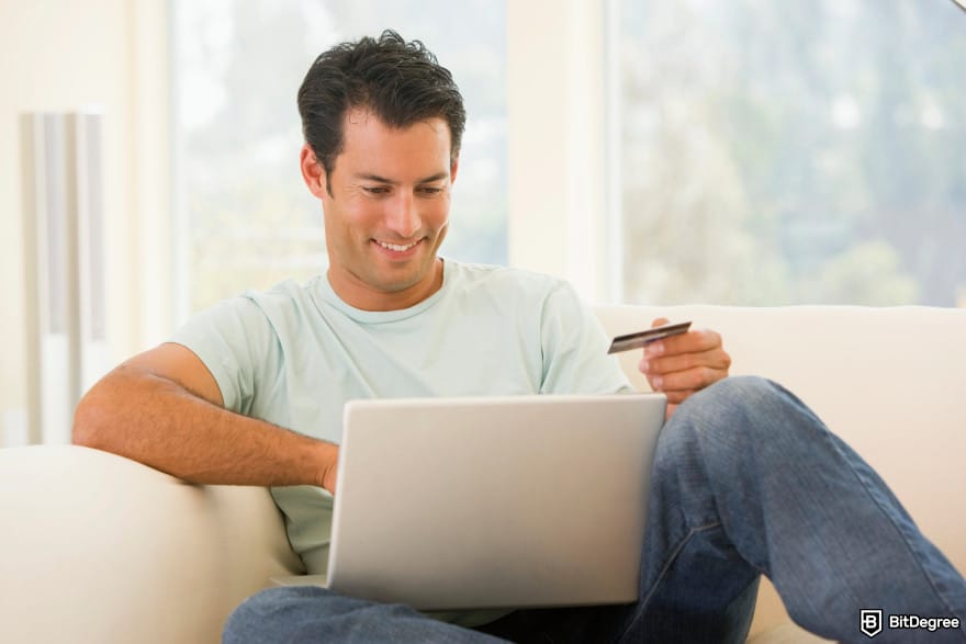 Is Ethereum dead: man in living room using laptop and holding credit card.