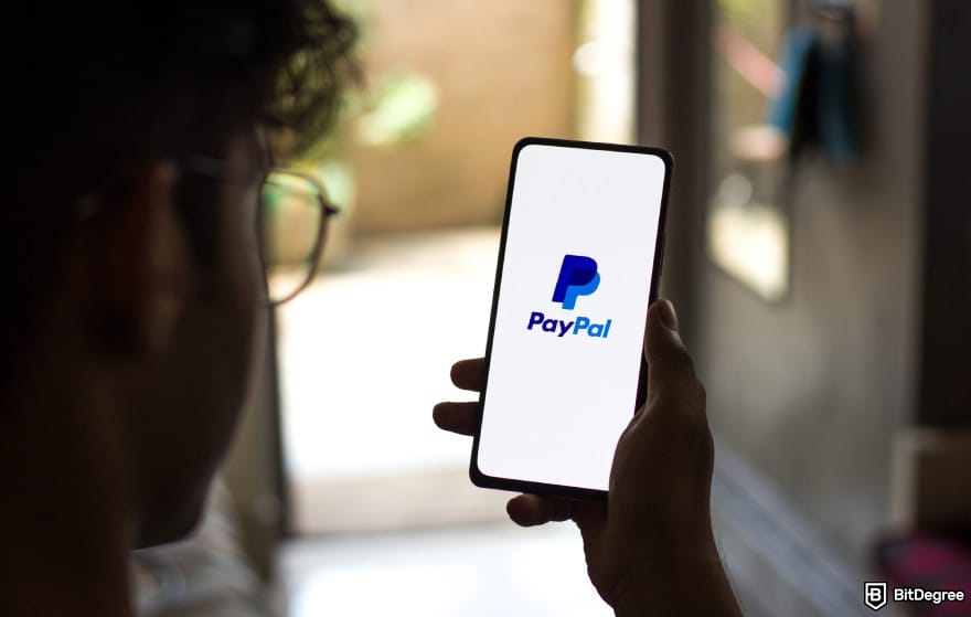 Is PayPal available in India: man holding smartphone with PayPal logo.