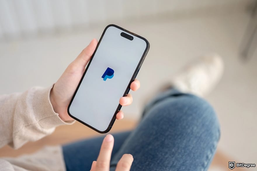 Is PayPal available in Pakistan: someone holding a phone displaying a PayPal logo.