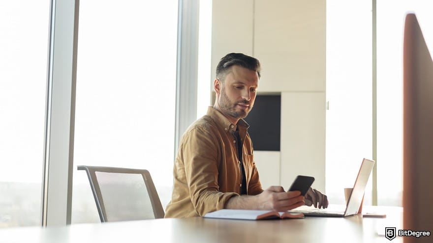 Is Robinhood safe: a person looking at his mobile phone while sitting in front of a laptop.