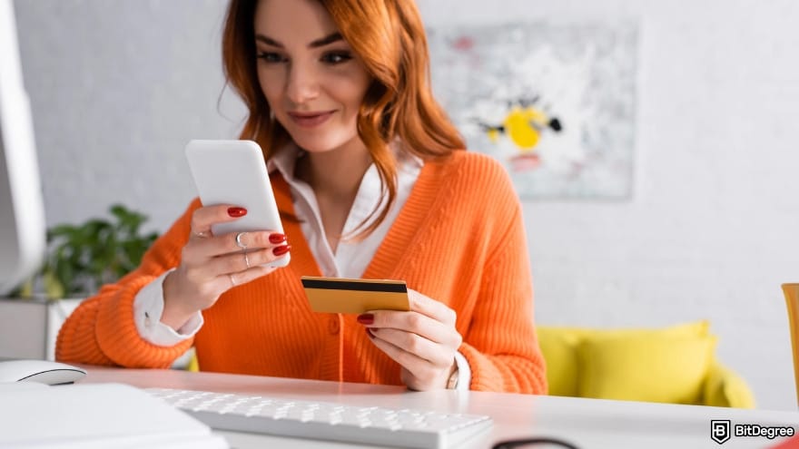 Is Wise available in Pakistan: a woman smiling while holding card near keyboard at home.