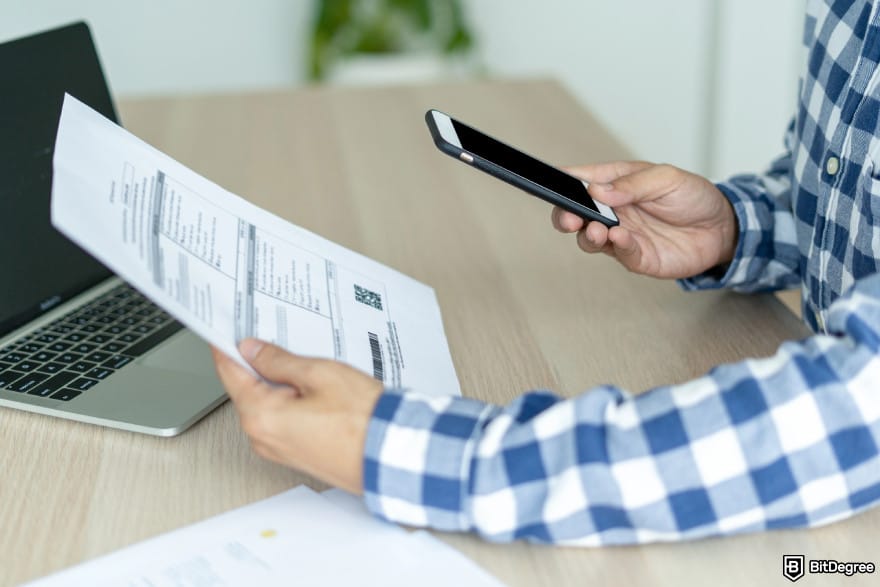 KuCoin KYC requirements: a man capturing document image with phone for verification.