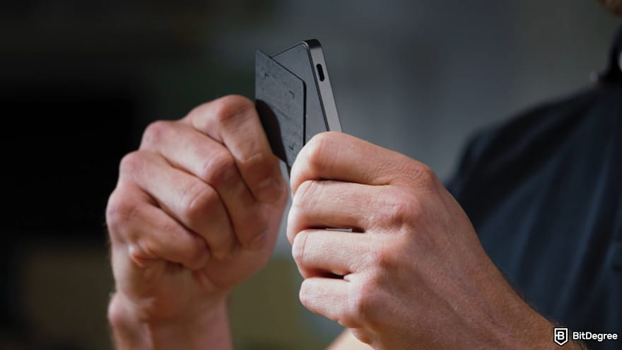 Ledger Recovery Key review: close-up of a person holding a Ledger Recovery Key and tapping it against a Ledger device.