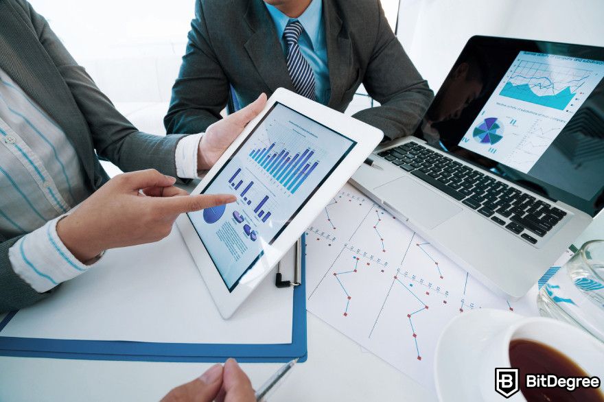 Lido staking: a group of business individuals engaged in a discussion while using a tablet and laptop.