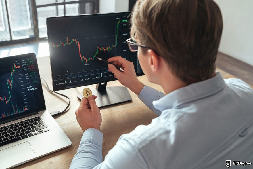 Managing multiple crypto wallets: a person holding a Bitcoin physical coin while analyzing a trading chart.