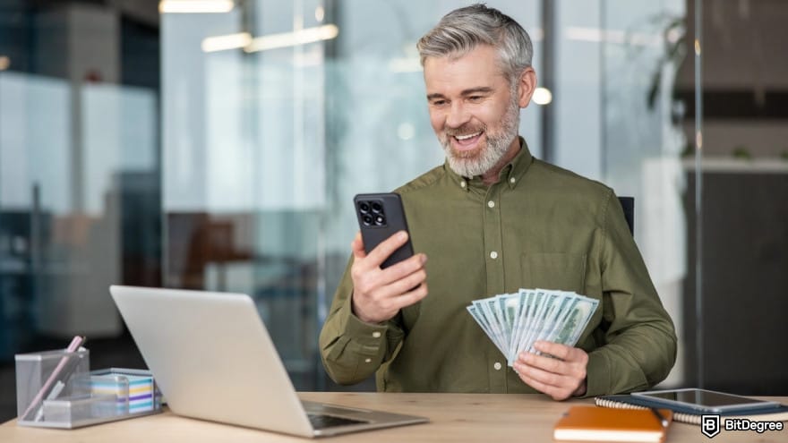 MEXC fees: a person sitting holding a smartphone and fanned hundred dollar bills. MEXC fees: a person sitting holding a smartphone and fanned hundred dollar bills.