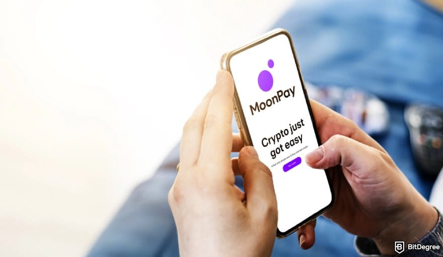 MoonPay review: a pair of hands holding a phone displaying MoonPay logo.