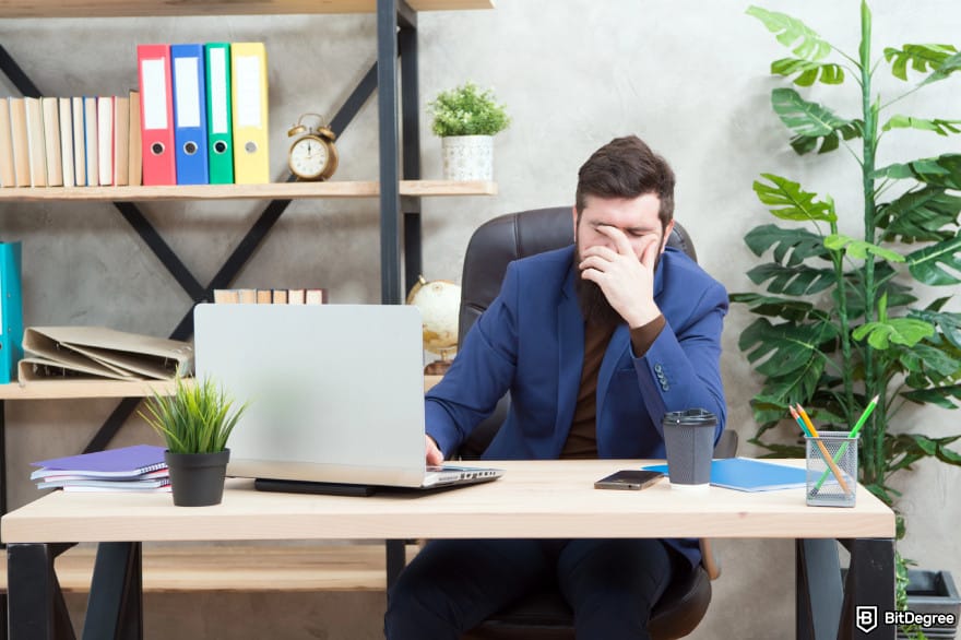 Most asked crypto questions: a man siting at a table with computer and face palming.
