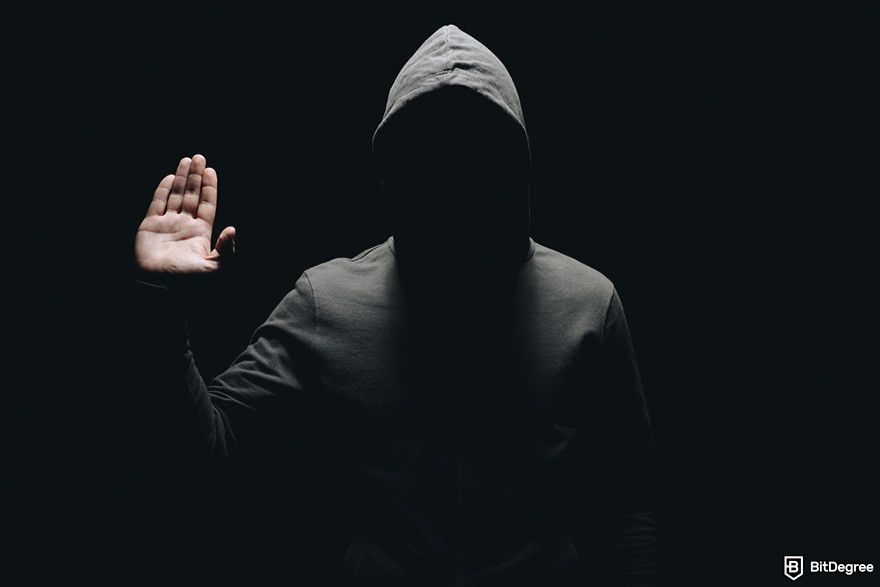 Next crypto to hit $1: a person wearing hoodie standing in the dark while raising one hand.