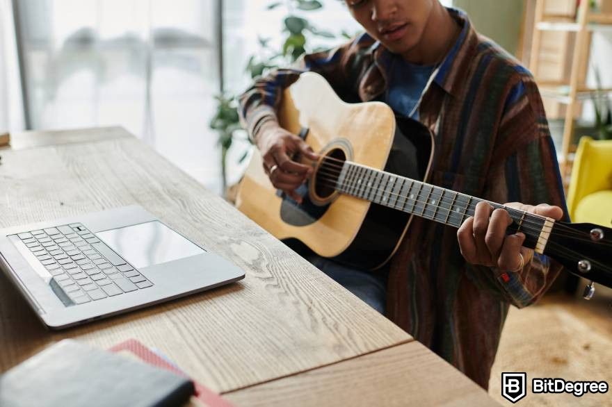 NFT âm nhạc: Nhạc sĩ biểu diễn với cây đàn guitar trước máy tính xách tay.