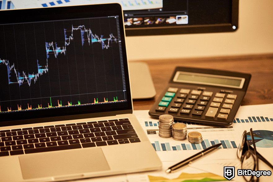 Notcoin Bybit: a laptop showing chart with a calculator, stacks of coins, a pen, and a pair of glasses on a table.