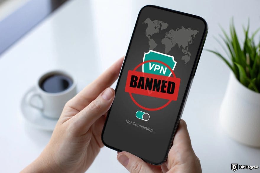 Polymarket review: two hands holding a phone showing VPN interface with the stamp "Banned" over it.