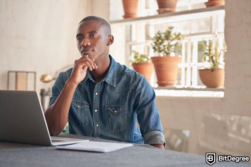 Pump and dump crypto: A man at a table in front of a laptop thinking about something