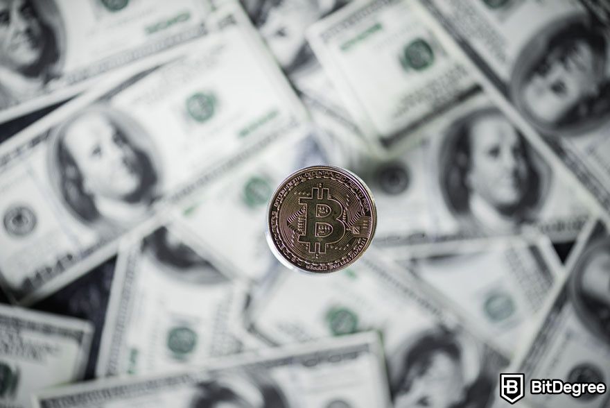 Should I buy Bitcoin: Bitcoin token centered over a blurred background of US dollar bills.