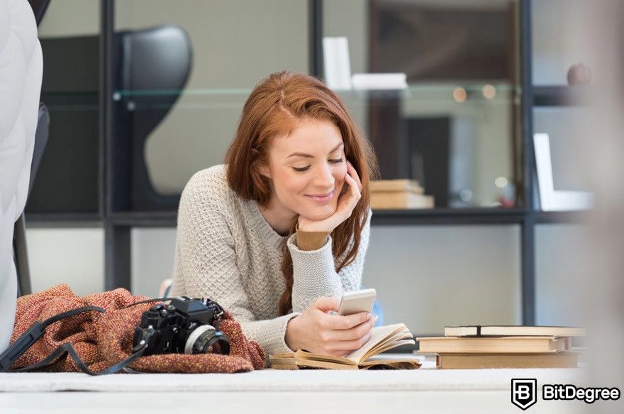 O que é token gating: uma mulher lê algo no telefone alegremente.