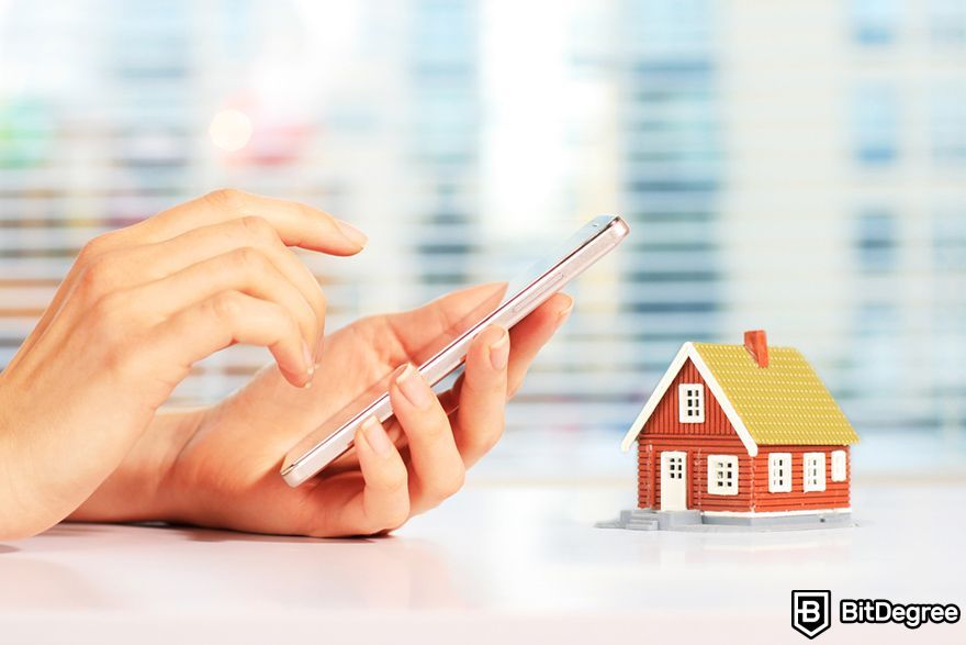 Tokenized real estate: a person holding a phone next to a house minature.