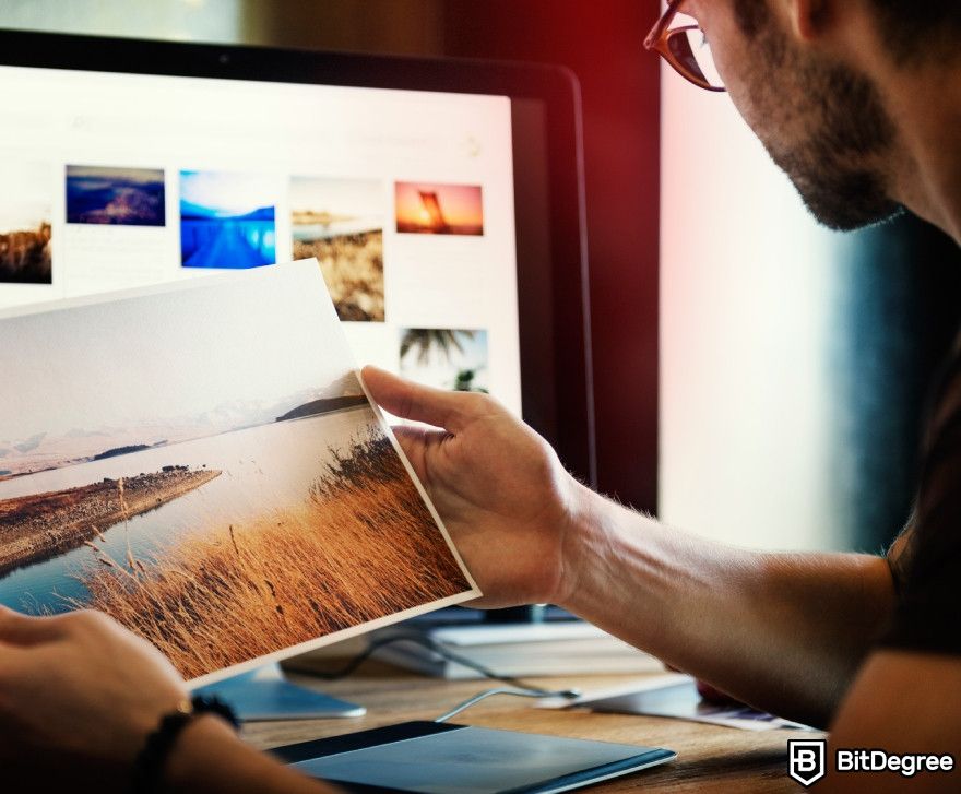 Topaz Photo AI review: A man holding a picture while looking at his computer.