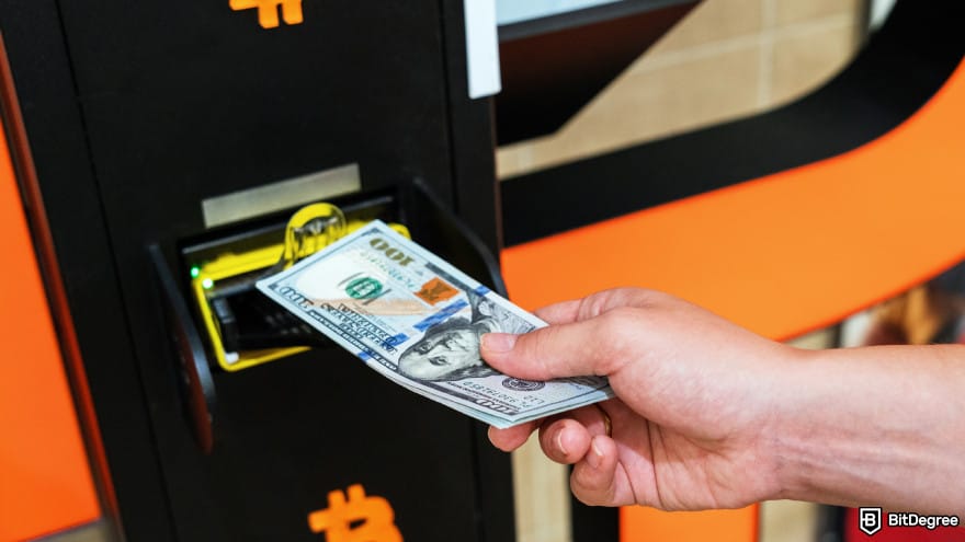 Uphold fees: a person inserting dollar bills into a Bitcoin ATM.