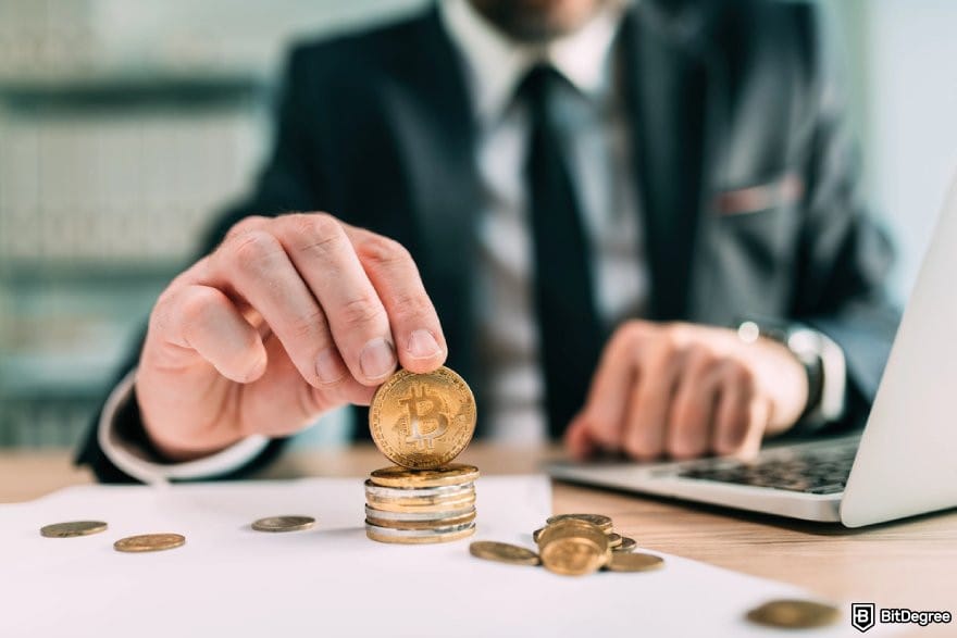 Uphold review: a man in a suit stacking Bitcoin and other coins.