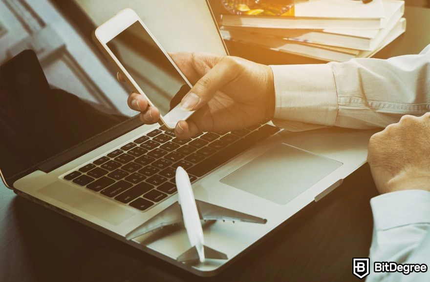 Virtual currency: A person using a phone near a laptop and a plane miniature.