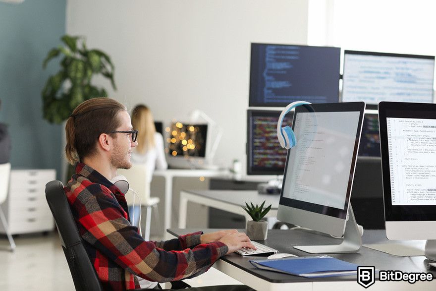 Web3 jobs: a person works on a computer with code on the screen in a modern office with multiple monitors.