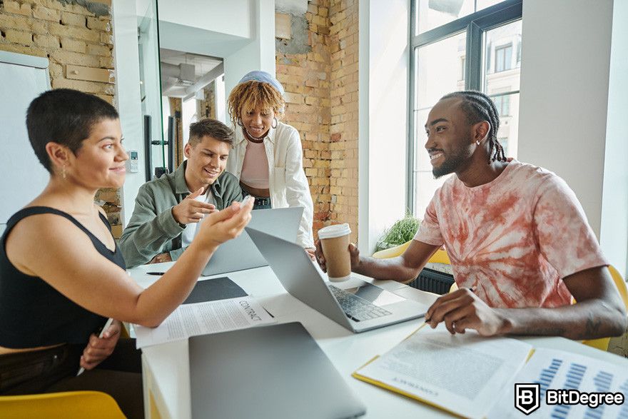 Web3 jobs: four people having discussion and working on laptops in a modern office setting.