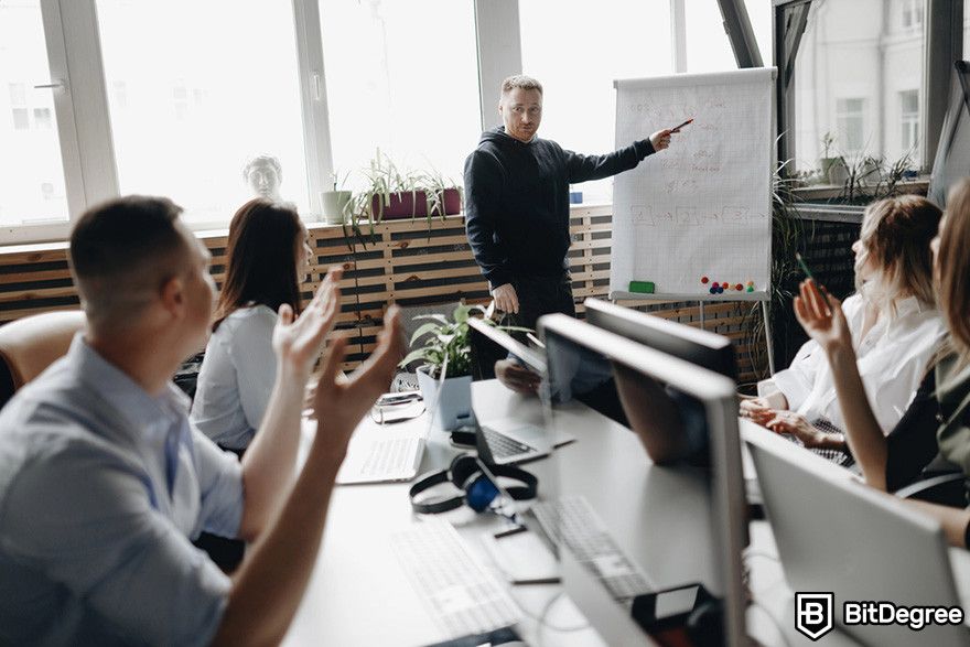 Web3 jobs: a person presenting a chart in front of a group of people in an office setting.