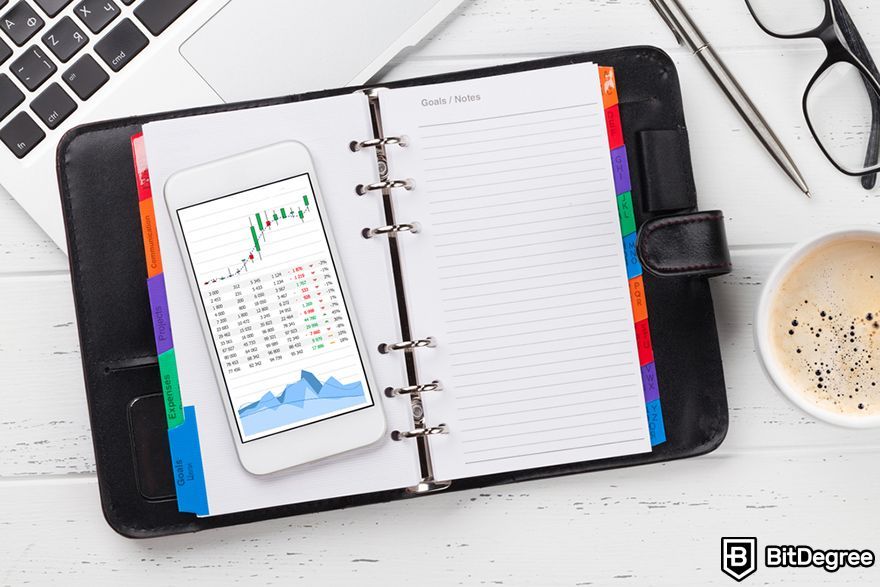 What is a trading journal: a notepad and a phone with a trading chart.