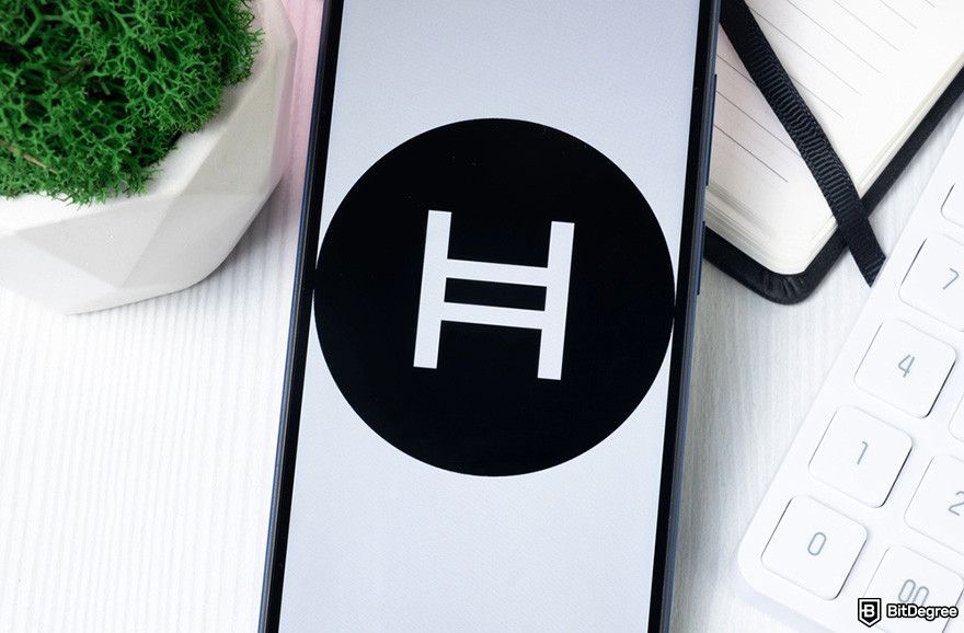 What is Hedera: a mobile phone displaying Hedera logo, a keyboard, and a notebook.