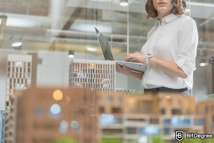 What is Render crypto: a person holding a laptop looking at a diorama of buildings.