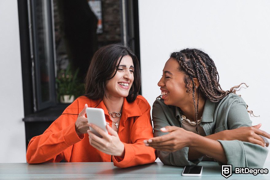 Where to buy BOOK OF MEME coin: two people laughing while pointing at a mobile phone.