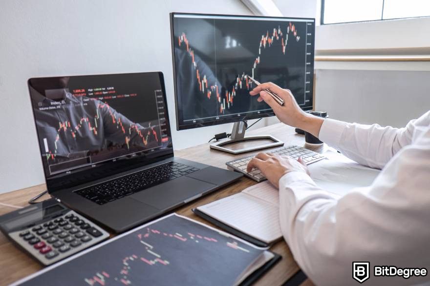 Will crypto recover: A person sitting at a desk with two monitors showing market graphs