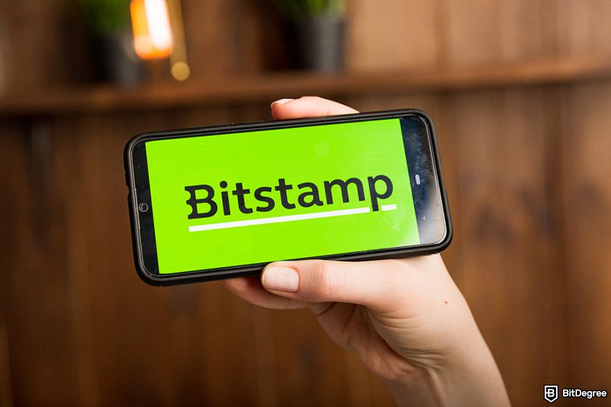 Bitstamp withdrawal: a person holding a smartphone displaying the Bitstamp logo.