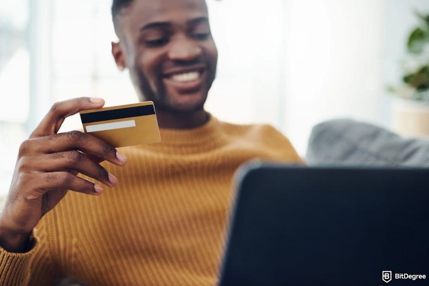 WorldRemit review: a person smiling while holding a payment card and using a laptop. WorldRemit review: a person smiling while holding a payment card and using a laptop.