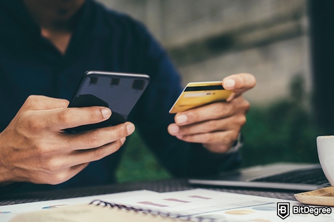 Best online finance degree programs: a man is holding a phone in one hand and a credit card in the other hand.