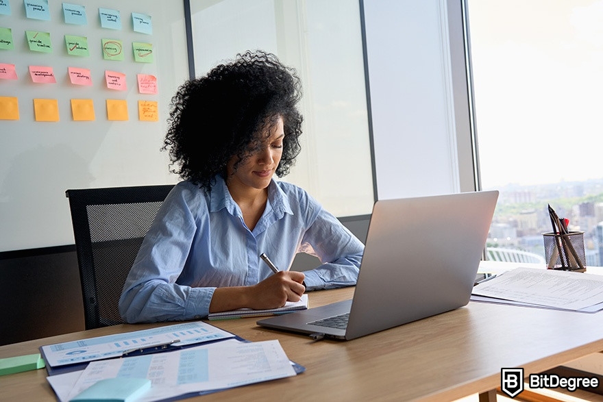 DataCamp SQL: a woman is sitting in front of a laptop and taking notes on a notepad.