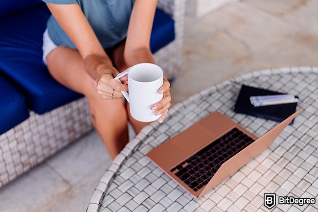 Distance learning: woman is sitting in front of a laptop and holding a cup.