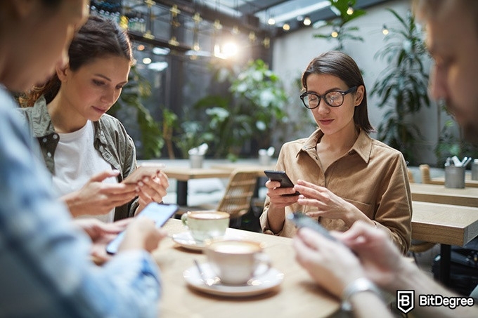 Online ethics courses: four people are sitting around a table and looking at their phones.