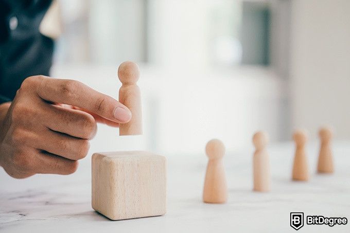 Online ethics courses: a man is placing a wooden figurine on a cube above other wooden figurines.