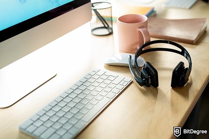 Online information technology degree: a desk with a monitor, keyboard, mouse, and headphones.