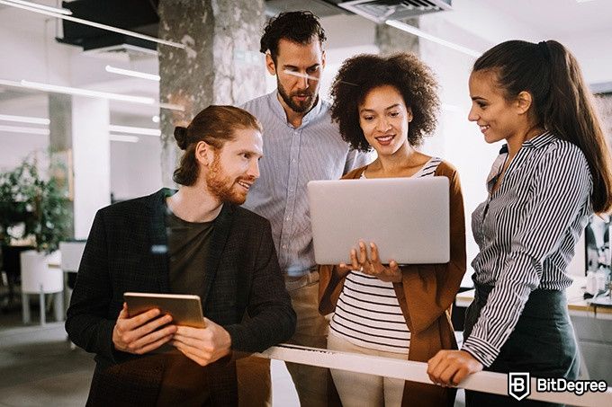 Online information technology degree: four people are standing and looking at a computer.