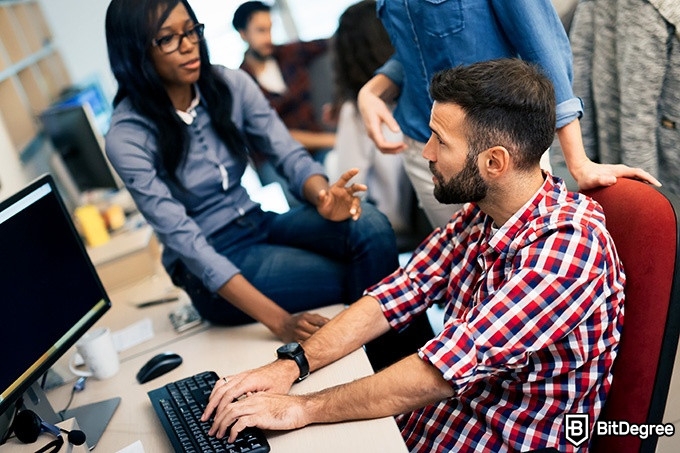 Online information technology degree: a woman is sitting on a desk and talking to a man.