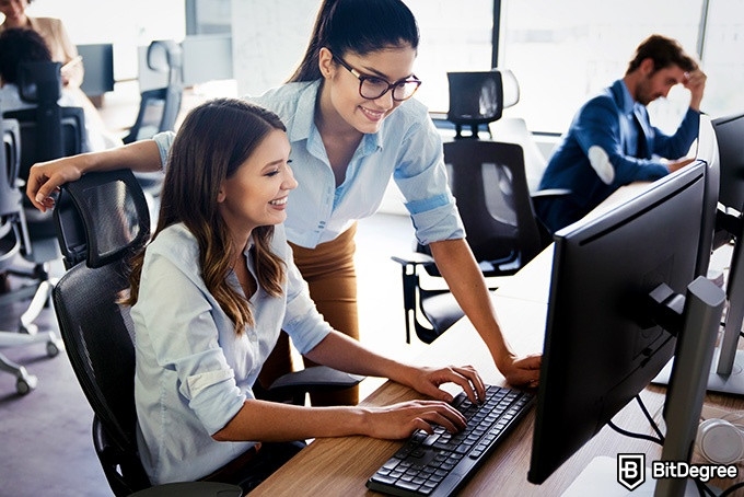 Online information technology degree: two women are looking at a computer screen and talking.