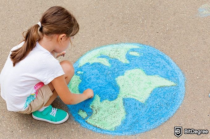 Online social sciences degree: a girl is drawing the globe with crayons on the pavement.