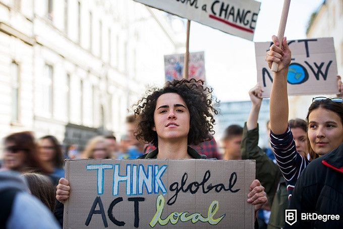 Online social sciences degree: a group of people protesting for change. A woman holds a sign that reads Think Global, Act Local.
