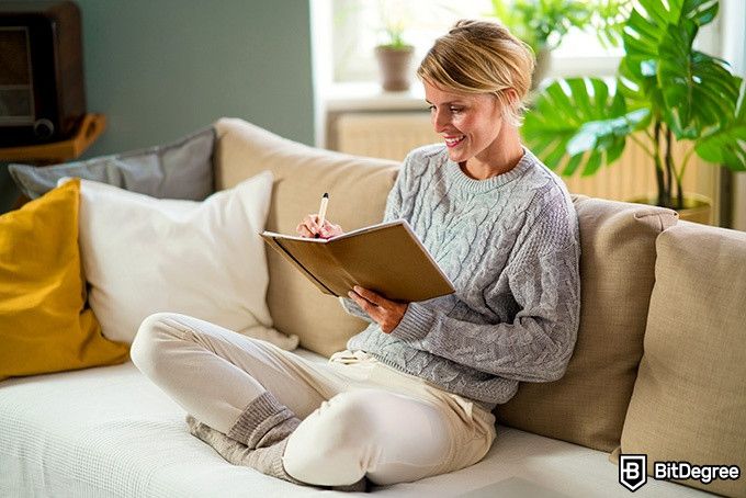 Online social sciences degree: a woman is relaxing on a couch and writing in a journal.